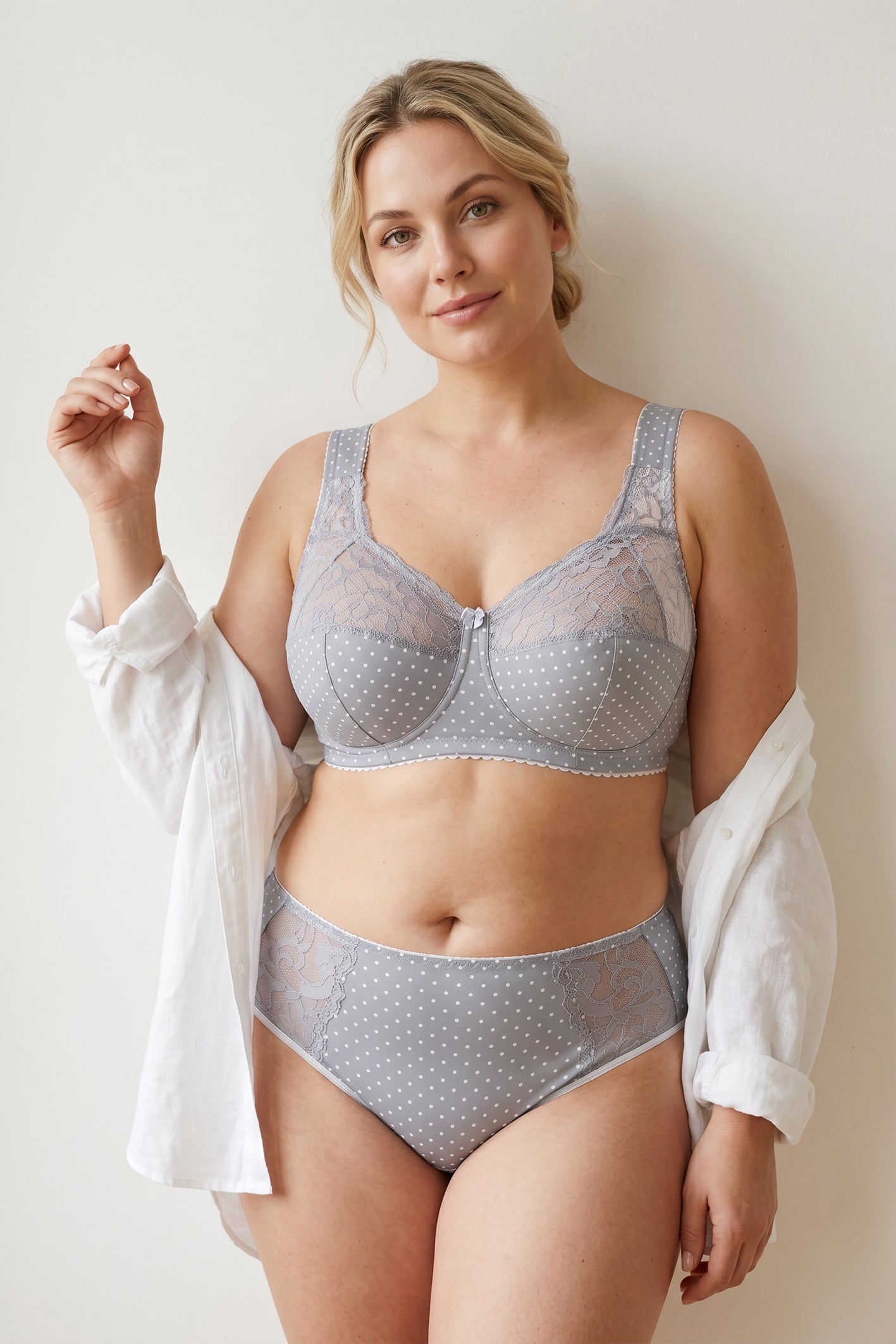 A plus-size blonde model wearing a light gray and white polka dot cotton bra with padded straps and matching mid-waisted briefs.