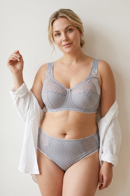 A plus-size blonde model wearing a light gray and white polka dot cotton bra with padded straps and matching mid-waisted briefs.