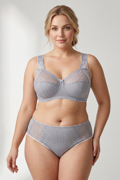 A plus-size blonde model wearing a light gray and white polka dot bra and matching mid-waisted briefs.
