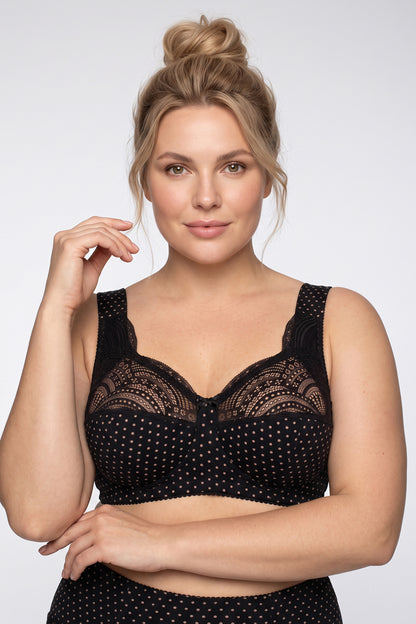 A woman modeling a black lace and polka-dot unpadded non-wired cotton bra with wide padded straps against a light gray studio background.